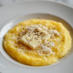 Creamy Polenta, served on a plate with butter, parmesan and fresh ground black pepper.
