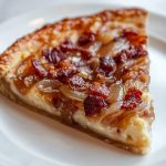 A slice of German Zwiebelkuchen (Onion and Bacon Pie), on a white plate.