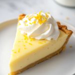 French Lemon Tart Slice with whipped cream and lemon shavings, served on a plate.