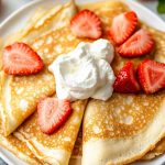 Homemade French Crepes, served on a plate with fresh strawberries and whipped cream.