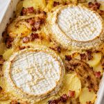 French Tartiflette with melted Reblochon cheese, sliced potatoes, bacon, and onions in a white baking dish.