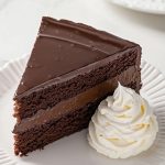 Sachertorte - Chocolate cake served with whipped cream, on a white plate.