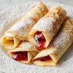 Palačinky, with strawberry jam, served on a white plate.