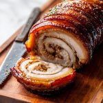 Porchetta (Italian Pork Roast), sliced and served on a wooden board.