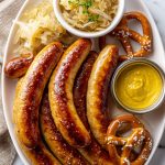 How to cook bratwurst served with beer onions, sauerkraut, mustard, and a pretzel.