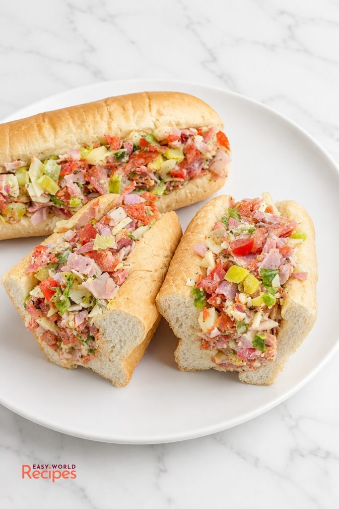 Two chopped Italian sandwiches in hoagie rolls on a white plate.